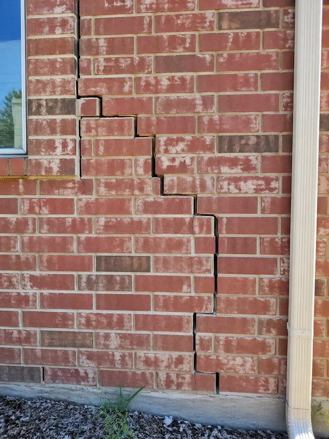 Severe stair step cracks in brick foundation caused by Dallas clay soil movement.