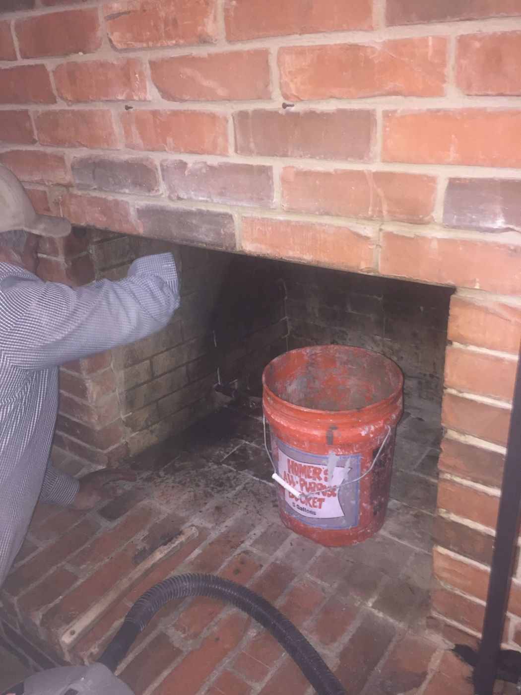 A technician is repairing and repointing the interior firebox brickwork of a residential fireplace