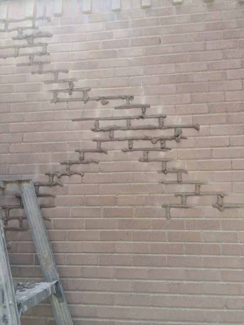 Diagonal brick crack repair Repair work in progress on a residential exterior wall featuring a diagonal brick crack. Old mortar joints have been cut out and fresh mortar has been applied to stabilize the stepped crack pattern.