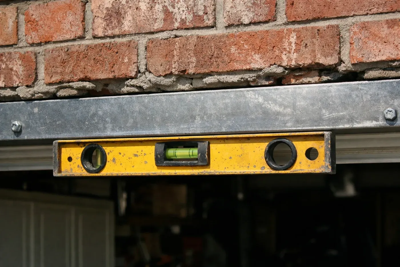 Professional garage lintel repair in Dallas showing a level to fix a sagging garage lintel and brick cracks.