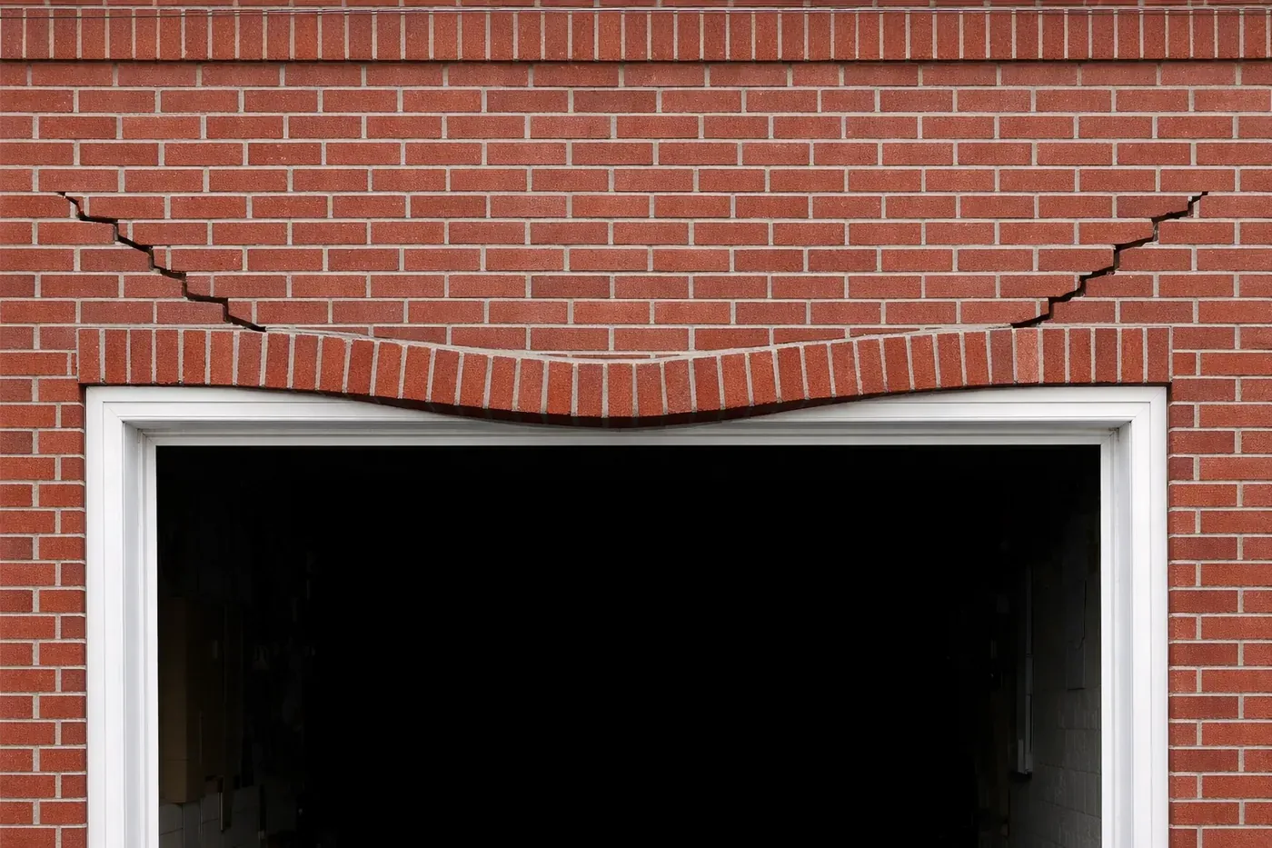 Sagging garage door lintel with stepped diagonal cracks in brick above opening