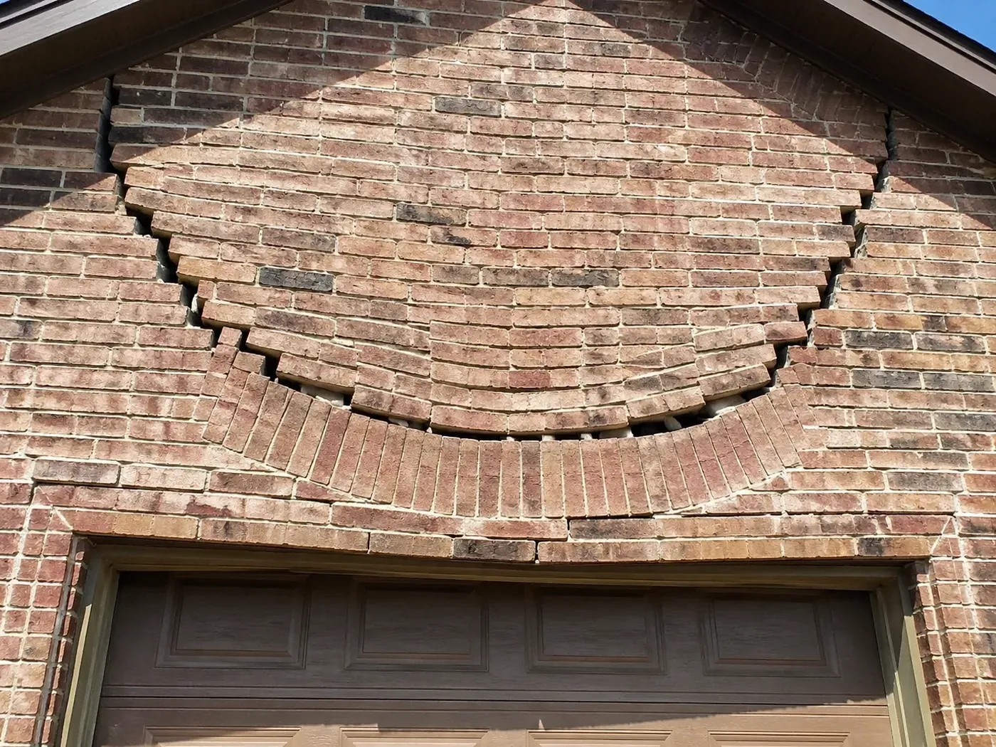 Bowing garage lintel repair Mesquite showing sagging bricks and stair-step masonry cracks.
