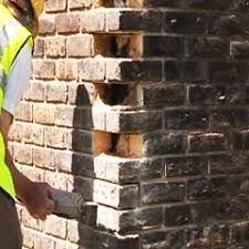 A technician assessing a damaged brick corner with missing and loose bricks